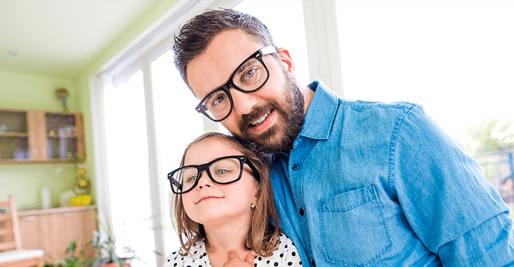A joyful moment shared between a father and daughter, both wearing glasses and smiling warmly at the camera.